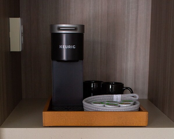 Keurig-kahvinkeitin, kaksi mustaa mukea ja spiraalimallinen vedenkeitin puulaatikossa.