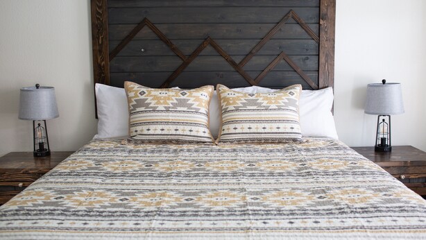 Una cama bien tendida con ropa de cama estampada, dos lámparas de noche y un cabecero de madera.