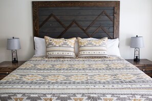 A neatly made bed with patterned bedding, two bedside lamps, and a wooden headboard. - Pine Lodge (Encampment)
