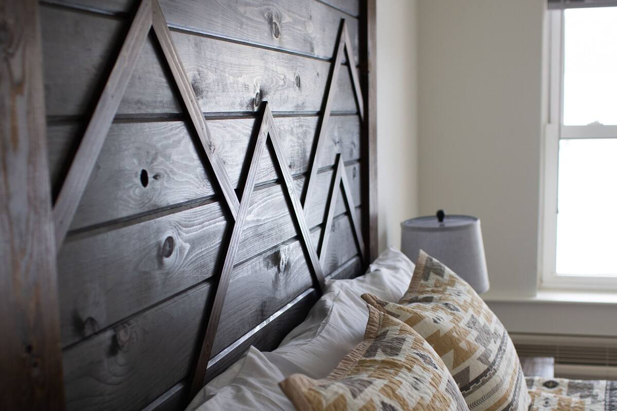Una cama con cabecera de madera, almohadas blancas con diseño y colcha estampada.