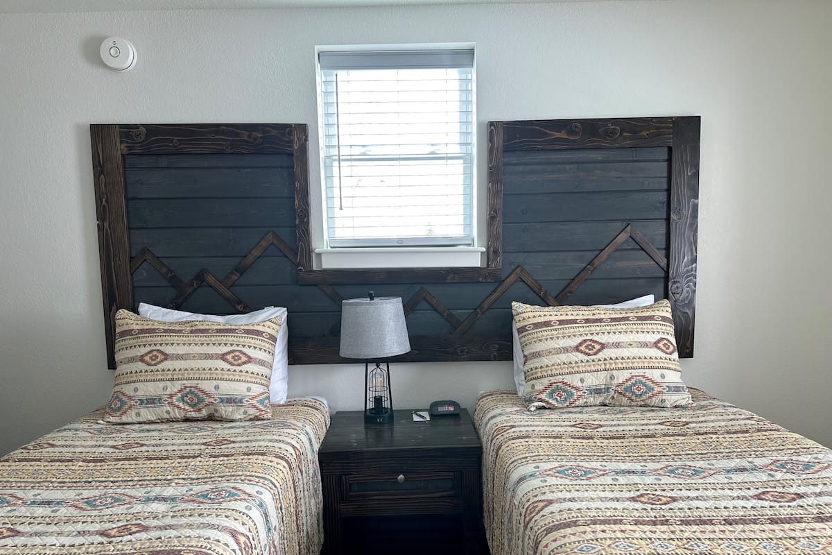 Un dormitorio con dos camas, una mesita de noche, una lámpara y una ventana.