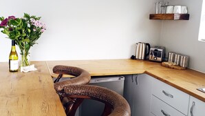 A kitchen with a wooden table, a chair with a unique design, and a wine bottle on the counter.