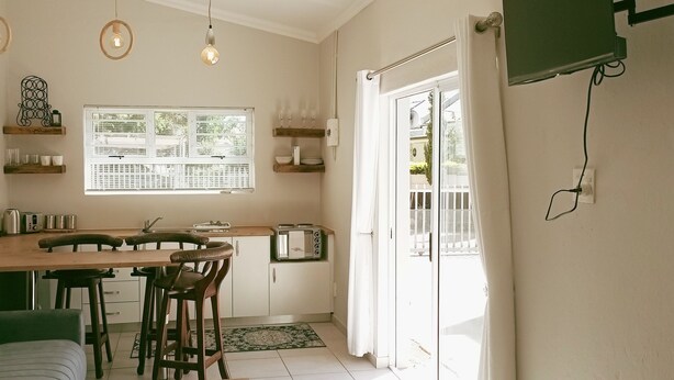 A compact kitchen with a dining table, bar stools, and a window with blinds.