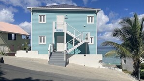 Un bâtiment à deux étages, doté d’un escalier menant à l’entrée, situé sur une route côtière et offrant une vue sur l’océan.