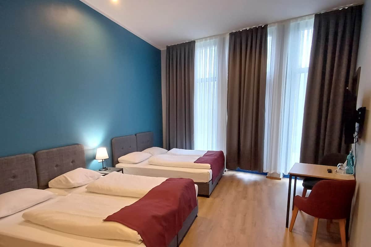 Quarto de hotel com duas camas, uma escrivaninha, uma cadeira, televisão e janela com cortinas.