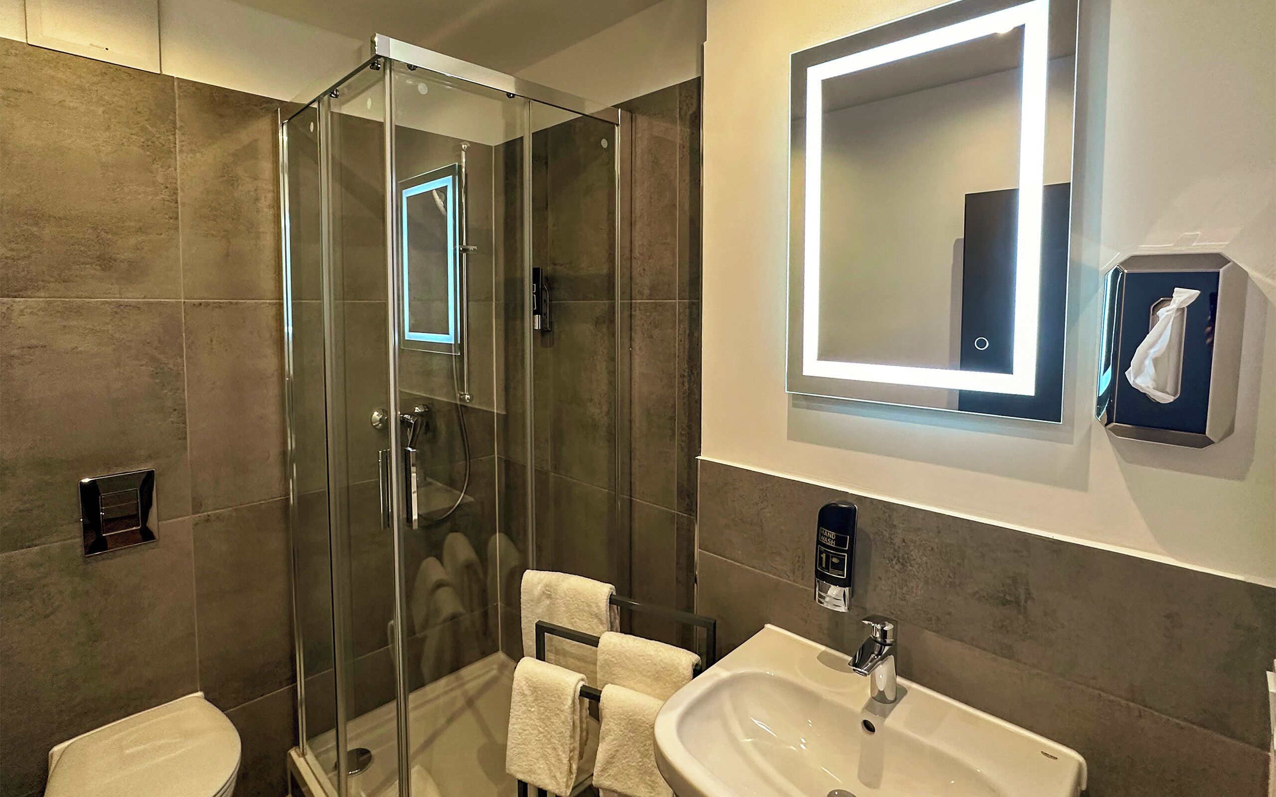 Une salle de bain moderne avec une douche à parois de verre, un lavabo, un miroir et un porte-serviettes.
