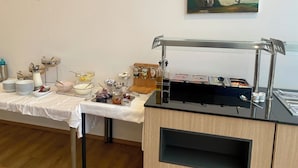 A buffet setup with various food items and condiments on a table, a painting on the wall, and a coffee machine. - Trip Inn Düsseldorf Neuss (Neuss)