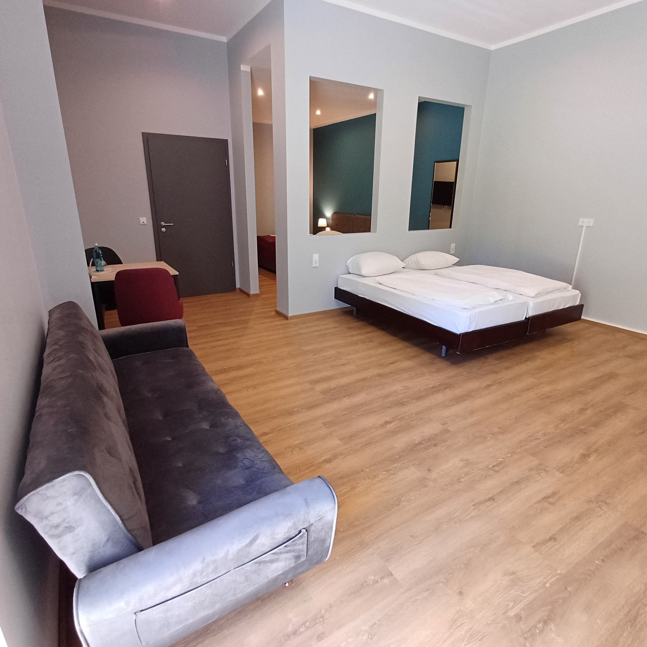 A modern, well-lit room with a large bed, a sofa, and a dining table.