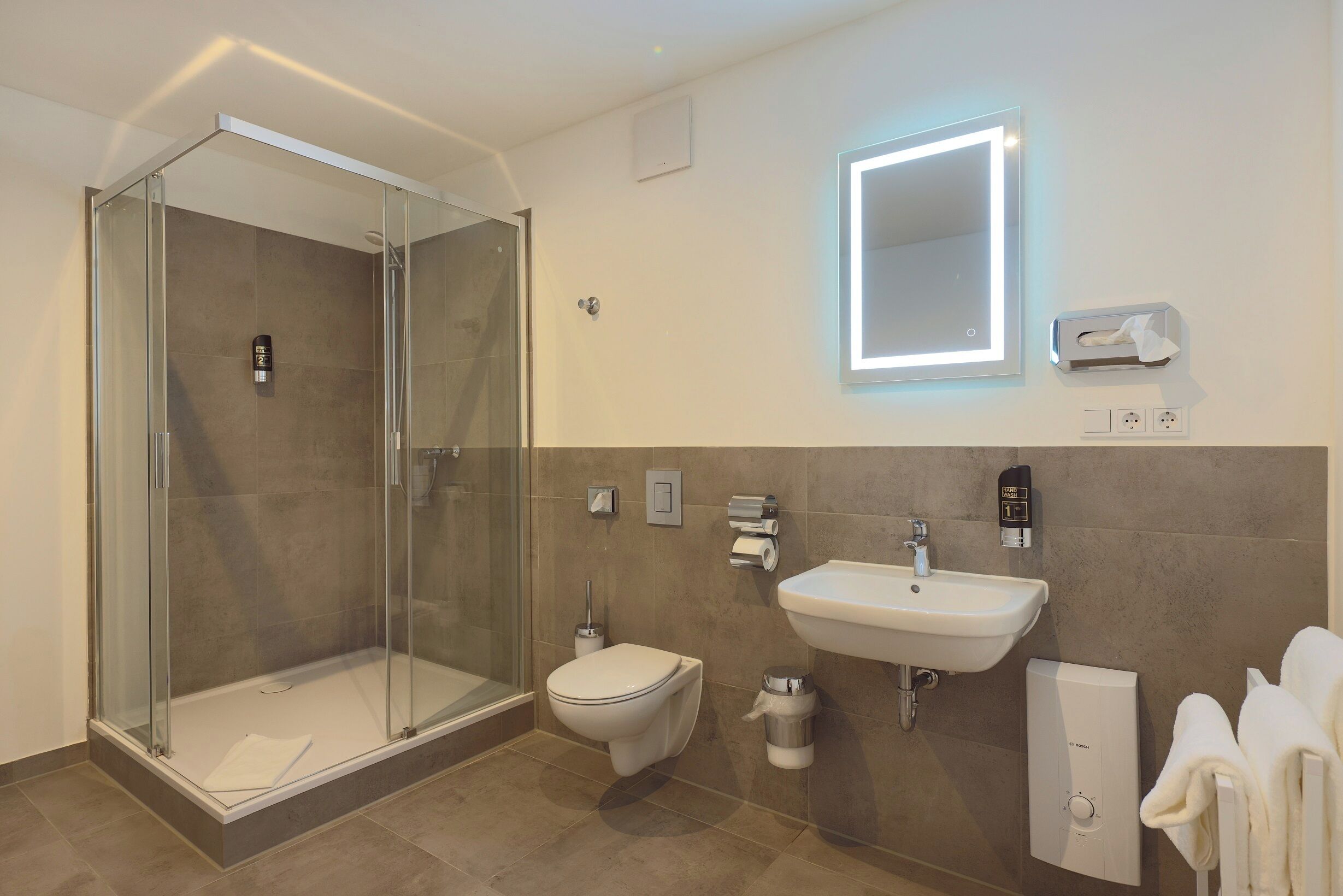 Un baño moderno con ducha envuelta en vidrio, inodoro, lavamanos y toallero.
