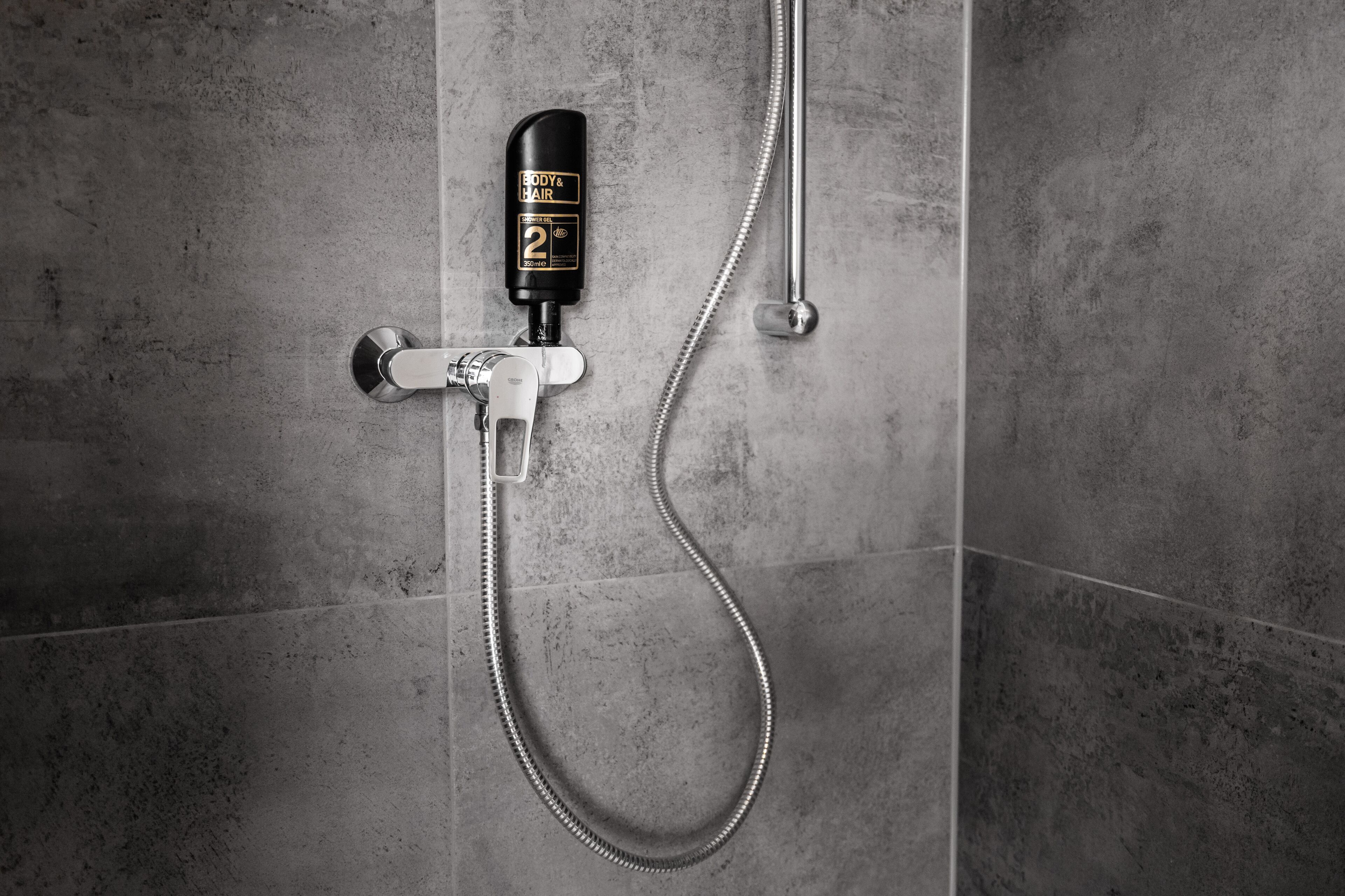 A shower with a handheld showerhead and a wall-mounted body & hair spray bottle.