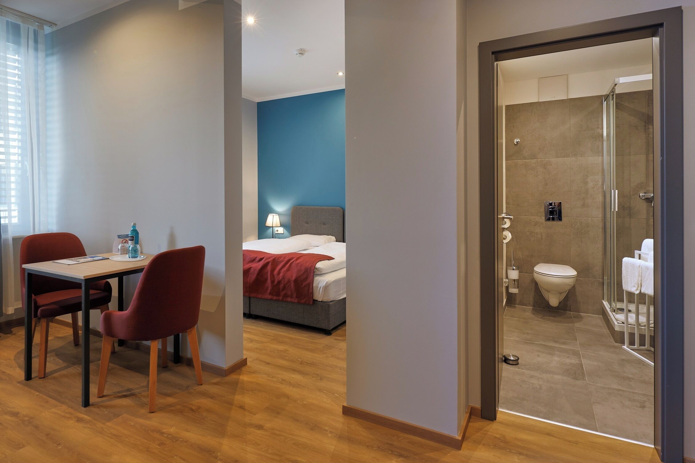 Een hotelkamer met een bed, een bureau met stoelen, en een badkamer met douche en toilet.