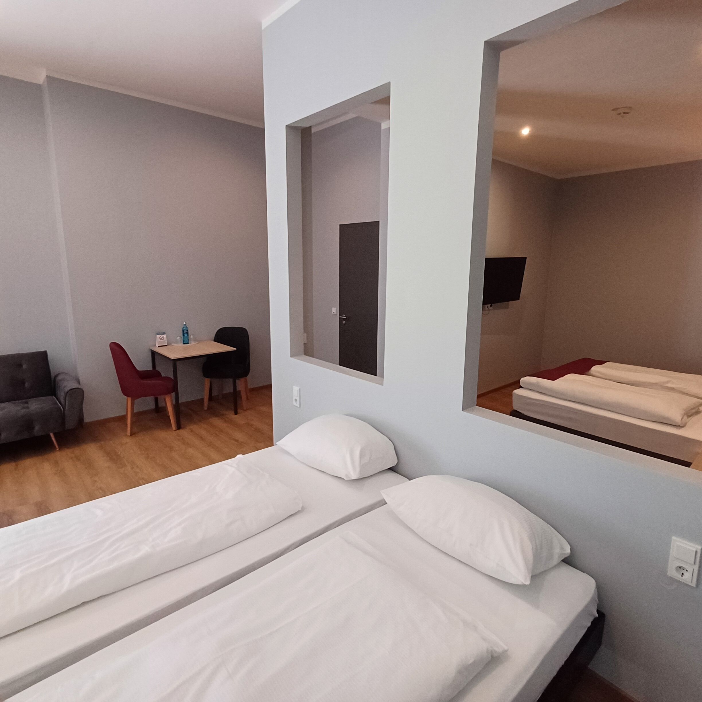 A hotel room with a bed, a desk with a chair, and a TV mounted on the wall.