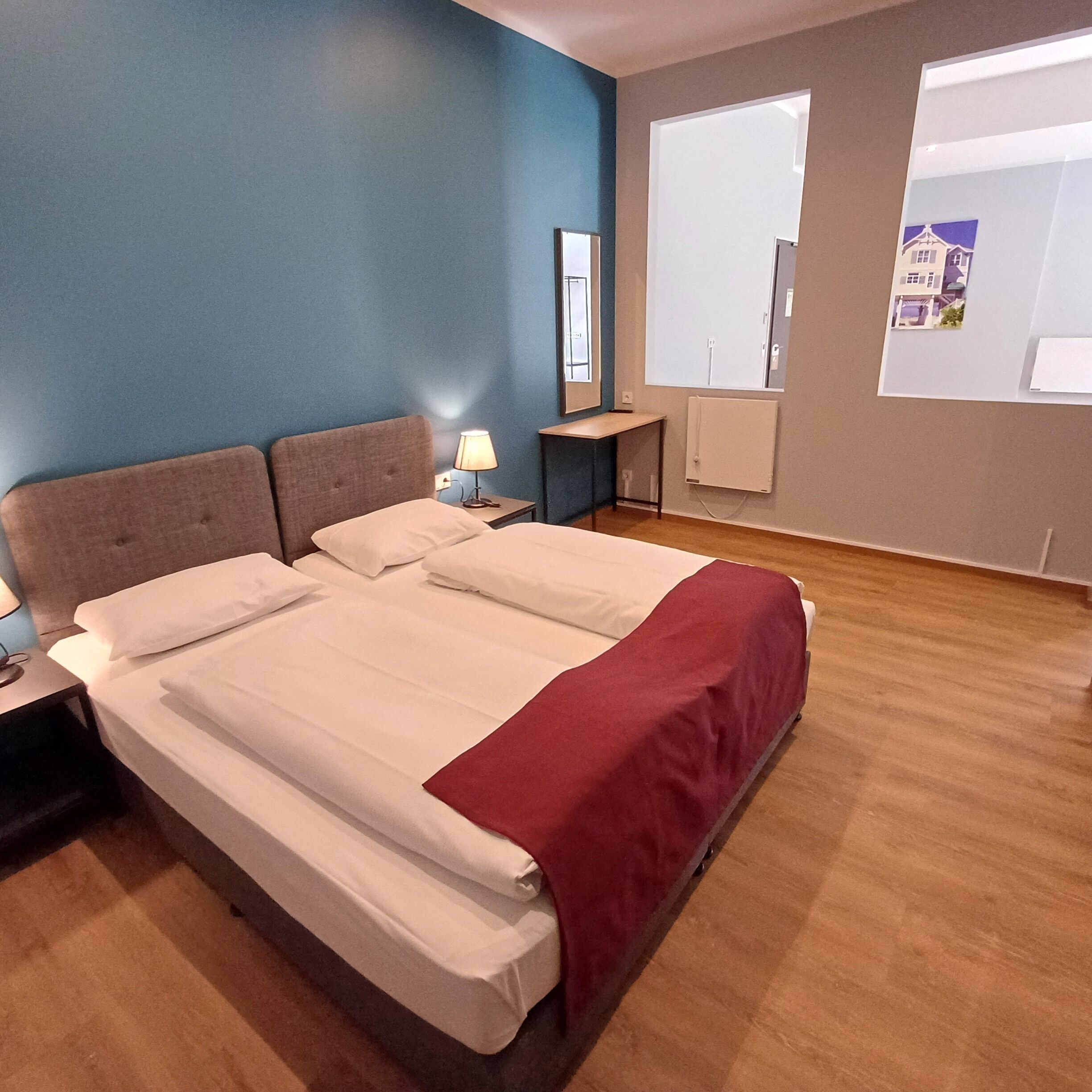 Una habitación de hotel con una cama grande, una mesita de noche, una lámpara, una ventana con vistas y un calefactor en la pared.