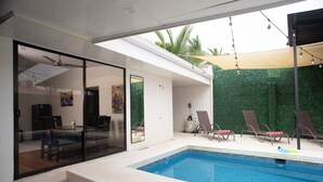 A modern outdoor swimming pool with a glass enclosure, lounge chairs, and a green wall backdrop. - Modern Villa Steps to Nightlife (Jacó)
