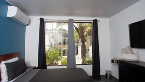 A hotel room with a bed, a TV, a window with curtains, a small trash bin, and a basket on the dresser. - Modern Villa Steps to Nightlife (Jacó)