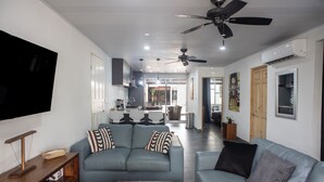 A modern living room with a grey sofa, a wooden coffee table, and a flat-screen TV mounted on the wall. - Modern Villa Steps to Nightlife (Jacó)