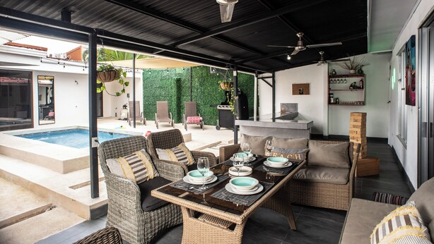 An outdoor patio with a dining table set for four, surrounded by wicker furniture, a pool, and a barbecue area. - Modern Villa Steps to Nightlife (Jacó)