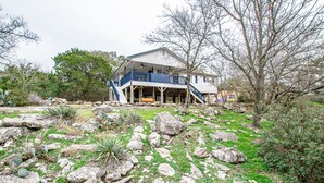 A two-story house with a balcony, surrounded by rocks and sparse vegetation.