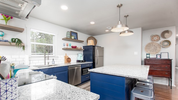 A modern kitchen with blue cabinets, a stainless steel refrigerator, and a granite countertop.