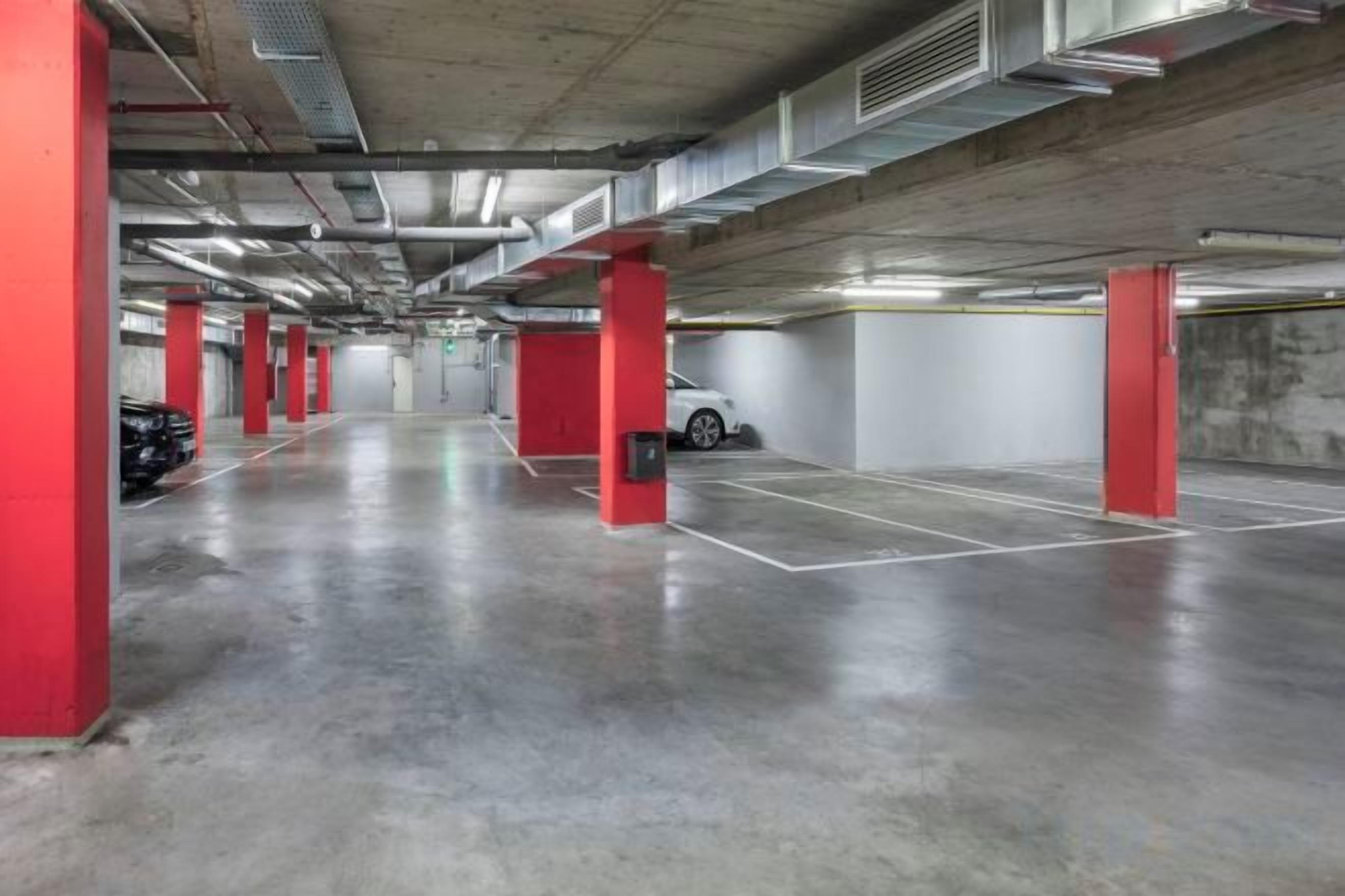 An indoor parking garage with concrete floors, red pillars, and white walls.