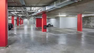 An indoor parking garage with concrete floors, red pillars, and white walls.