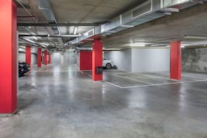 An indoor parking garage with concrete floors, red pillars, and white walls. - B&B Hotel Zaragoza Plaza Mozart (Zaragoza)
