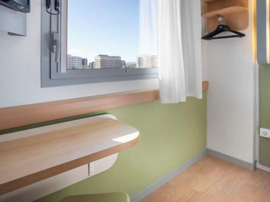 A room with a window, a bench, a hanging coat rack, and a green wall.