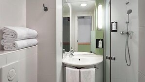 A modern bathroom with a white sink, a glass shower enclosure, and neatly folded towels on a shelf.