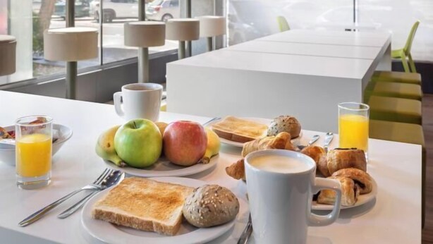 A breakfast setup with toast, croissants, muffins, and fruit on a table with a white tablecloth.