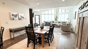 A spacious dining area with a wooden table and chairs, a large rug, and a view of the living room through a glass door. - Brooklyn Bridge Vacation Condo (Arnolds Park)