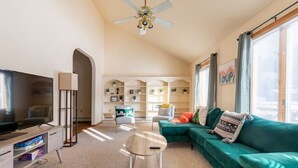 Un salon moderne avec un téléviseur à écran plat, un ventilateur de plafond, un canapé vert et une bibliothèque.
