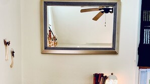 A room with a wooden desk, a white chair with a decorative backrest, a mirror, and a ceiling fan. - The Lookout - A Hill Country Cottage (San Marcos)