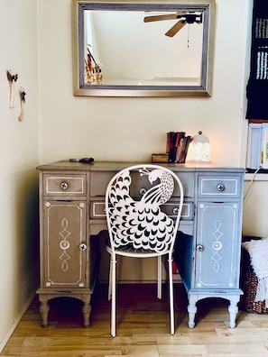 A room with a wooden desk, a white chair with a decorative backrest, a mirror, and a ceiling fan. - The Lookout - A Hill Country Cottage (San Marcos)