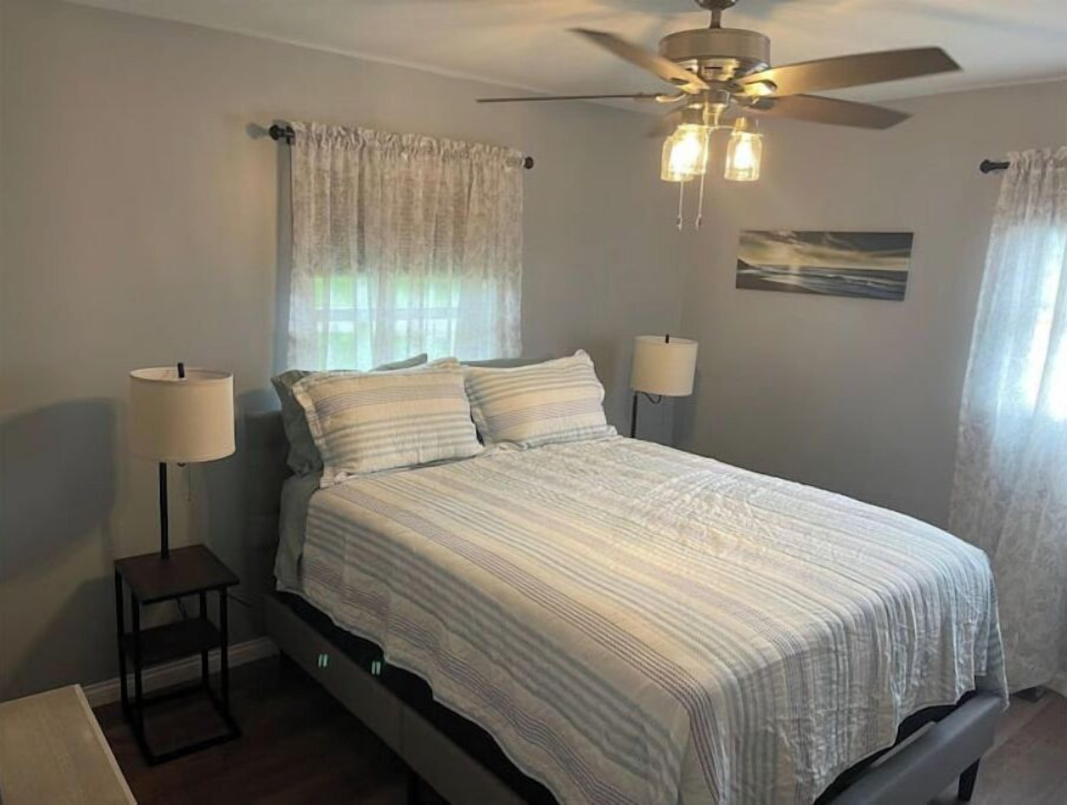 A bedroom with a bed, two bedside lamps, a ceiling fan, and a window with curtains.
