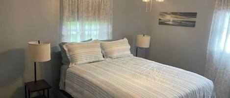 A bedroom with a bed, two bedside lamps, a ceiling fan, and a window with curtains.