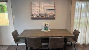 Ein Esszimmer mit einem rechteckigen Tisch, vier Stühlen, einer Blumenvase und einem Gemälde darüber.