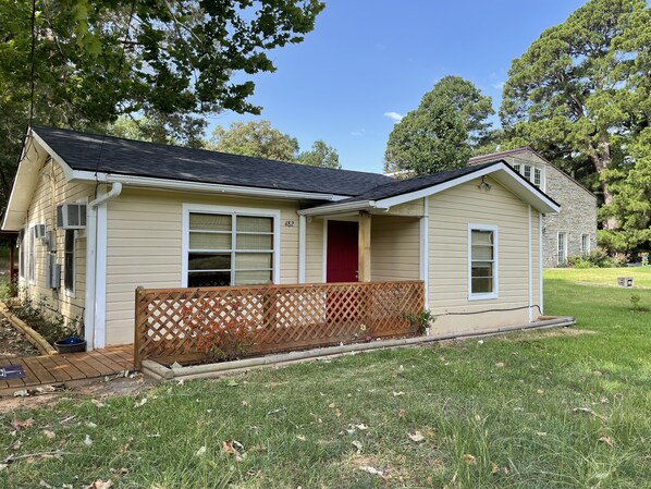 A single-story house with a red door, beige siding, and a small porch with a wooden lattice fence.
