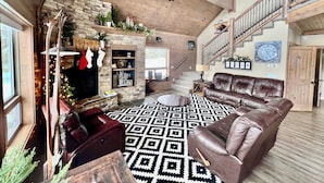 Un salón espacioso con chimenea, sofás de cuero, un tapete estampado y una escalera que sube a un nivel superior.