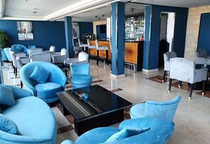 Un'ampia hall con comode poltrone rivestite in blu, un tavolino nero e un'area bar con scaffali pieni di bottiglie.