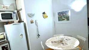 A compact kitchen with a microwave, refrigerator, and a small dining table with chairs. - Ap Copacabana 200m da praia – CP4 (Rio de Janeiro)