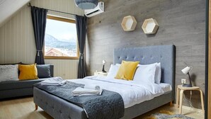 A modern bedroom with a large bed, a sofa, and a view of mountains through a window. - BOUTIQUE Hotel Entry E (Bansko)