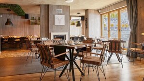 A spacious dining area with wooden tables and chairs, a fireplace, and large windows with curtains. - BOUTIQUE Hotel Entry E (Bansko)