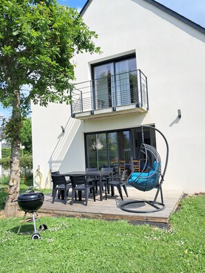 Ein modernes, zweistöckiges Haus mit Balkon, einer Hängematte und einem Grill.