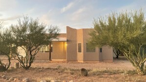 A modern house with a desert landscape, featuring a single-story structure, a large window, and a door. - Desert Ranch Home + 3 Horse stalls. Views of the Rincon Mountains (Tucson)
