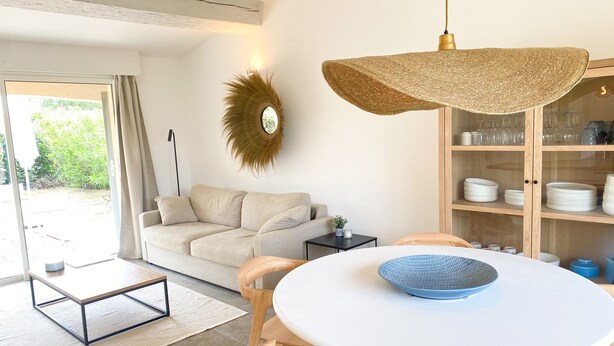 Een moderne woonkamer met een ronde witte tafel, een beige bank en een grote geweven hanglamp.