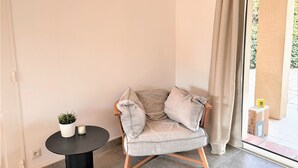 Een moderne woonkamer met een grijze fauteuil, een klein rond tafeltje met een plant en een groot raam met gordijnen.