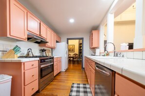Cocina compacta con armarios rosados, estufa, horno y lavavajillas.
