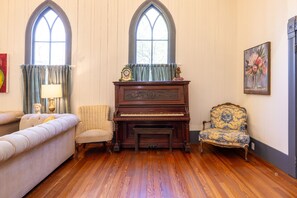 Una habitación con un piano de cola, dos sillones, un sofá y un ventanal con vistas.