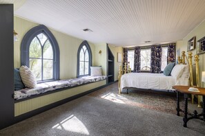 Un dormitorio con un amplio asiento junto a la ventana, una cama con cabecero decorativo y suelo cubierto de alfombra.