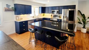 Une cuisine moderne avec des meubles de couleur bleu foncé, des appareils en acier inoxydable et un îlot central doté de tabourets de bar.